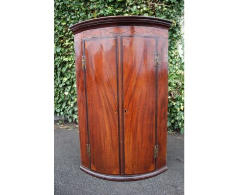 A George III mahogany bow-fronted corner cupboard, the doors inlaid with shell corners, the frieze with foliage inscribed dec