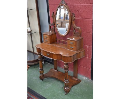 A Victorian mahogany serpentine fronted dressing table of small proportions; oval mirror supported by carved leafy scrolls ab