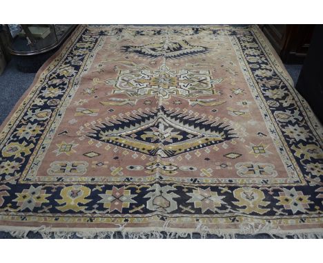 A hand woven carpet, geometric designs in hues of grey, cream and gold on a terracotta ground. 317cm x 274cm