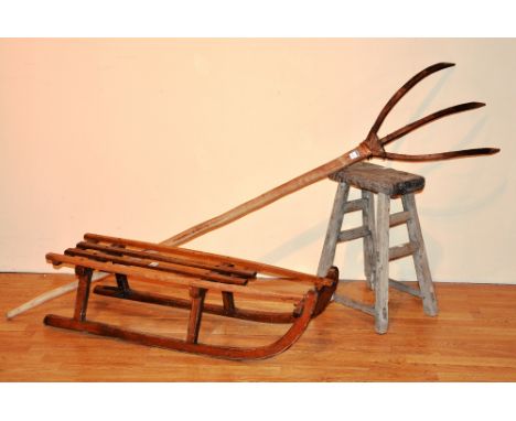 A vintage wooden sleigh, 24cm high x 99cm long, together with a rustic wood stool, 54cm high, and a wooden hay fork (3)