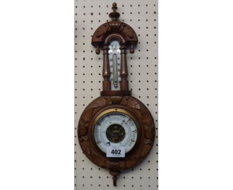 A late Victorian decorative carved walnut cased wall barometer/thermometer with printed ceramic scale and visible aneroid wor