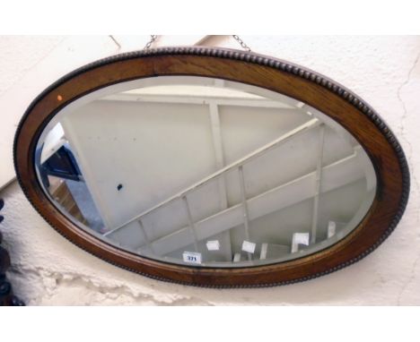 An early 20th Century polished oak and beaded framed bevelled oval wall mirror