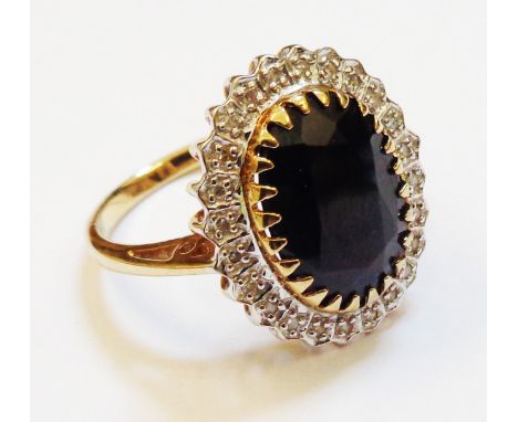 A hallmarked 375 gold ring, set with large central oval dark sapphire within a diamond encrusted border