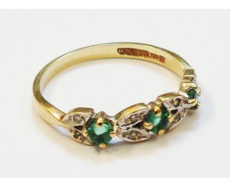 A yellow metal ring set with three small emeralds interspersed with pairs of tiny diamonds