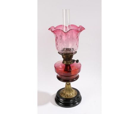 Late Victorian cranberry glass oil lamp, having cranberry glass shade and font, raised on brass column and circular ebonised 