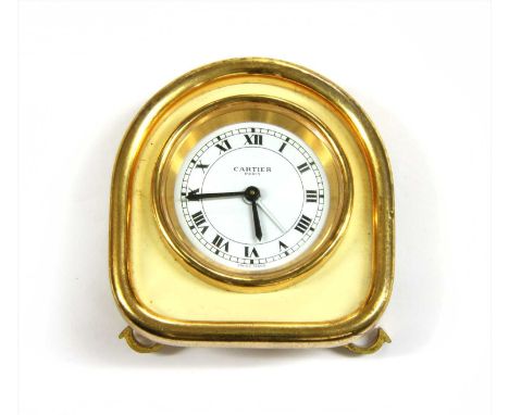 A Cartier gilt metal travel alarm clock, white dial with black Roman numerals, cream lacquer surround, hinged stand with feet