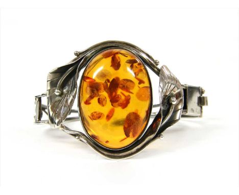 A sterling silver hinged amber bangle, with an oval cabochon amber, rub set to the top half with foliate surround, to wire lo