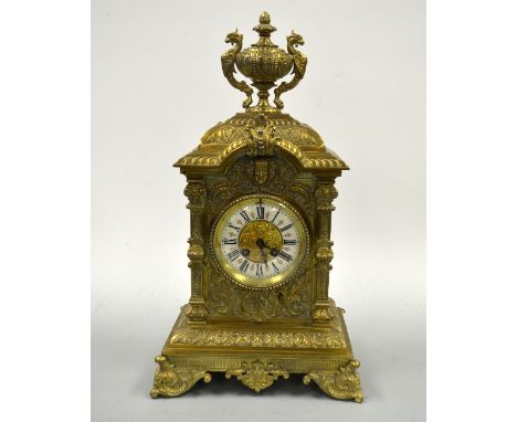 A GILT METAL MANTEL CLOCK, with circular porcelain dial with Roman numerals, eight day, urn finial with griffin mounts, scrol