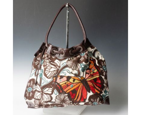 Beige canvas tote decorated with brown flowers and giant stitched butterfly. Brown leather straps and edging. Brown spotted c
