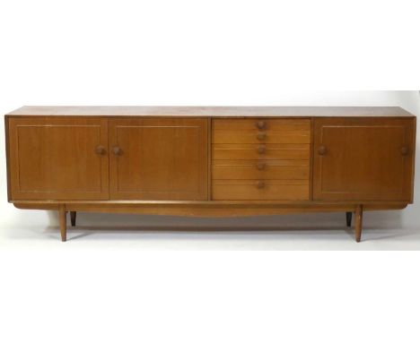 A 1960s teak long sideboard, having five graduated drawers flanked by a single fall-front compartment and a pair of cupboard 