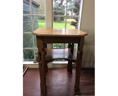 An Arts &amp; Crafts oak square table with curved hedges, raised on carved panelled supports with a shelf supported by stretc