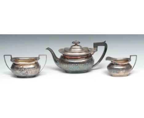 A George V silver three piece half-fluted boat shaped tea service, comprising teapot, milk jug and sugar basin, hinged domed,