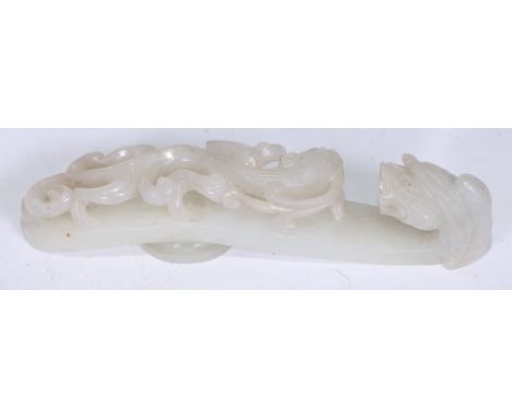 A Chinese pale celadon/white jade belt hook, late Qing dynasty, of typical serpentine form, carved and pierced with chilong c