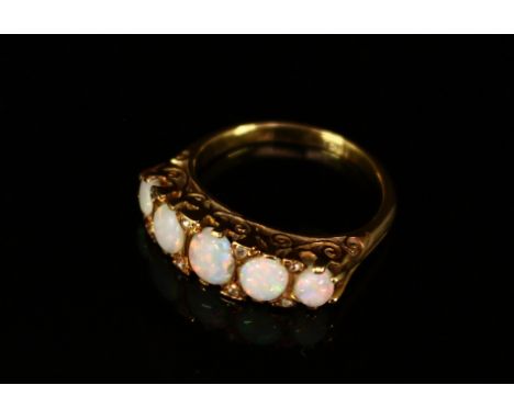 An 18ct gold five stone polished oval opal cabochon ring, each graduated stone divided by diamond accents, within an open scr