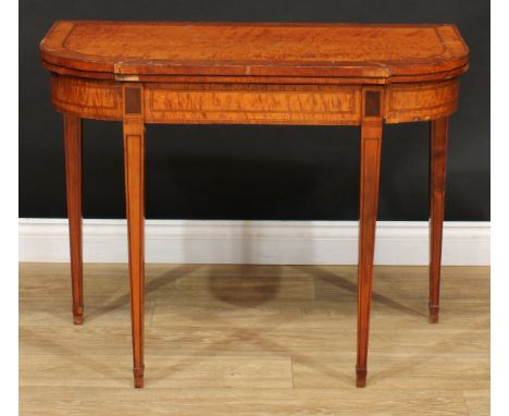 A George III satinwood card table, rounded rectangular break-centre folding top enclosing a baize lined playing surface, abov