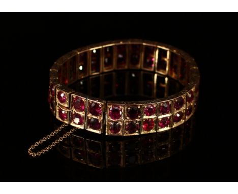 An early 20th century ruby and gold coloured metal articulated panel bracelet, set in two rows of circular cut stones, sprung