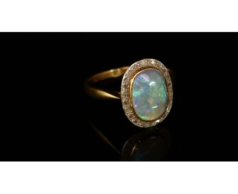 A gold and opal ring, the unmarked shank probably 18ct gold, the central polished oval opal cabochon surrounded by diamond ac