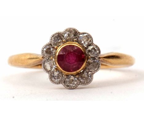 An 18ct ruby and diamond cluster ring, the circular cut faceted ruby bezel set in a surround of ten small diamonds in a flowe