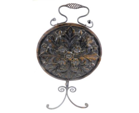 A heavily carved early 20thC oak firescreen, with metal mounts on a wrought iron stand with scroll front, the whole surmounte
