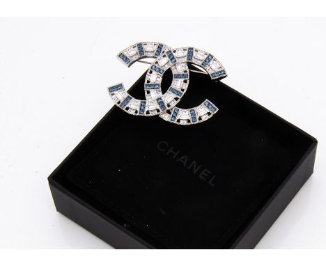 A paste set Chanel logo brooch, in blue and colourless step cut stones, with oval mark to base, in fitted fold out pouch and 
