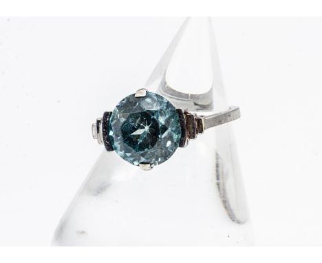 An Art Deco white metal zircon dress ring, the circular cut blue zircon in a four claw clamp setting with stepped shoulders, 