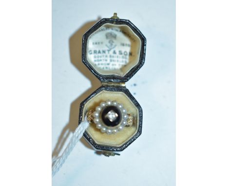 A 19th Century mourning ring, the black enamel dome centred by a diamond, surrounded by a bezel of half pearls, on scrolling 