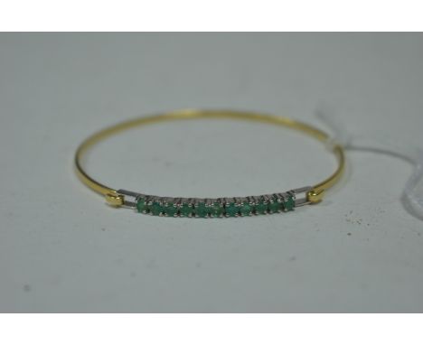 An emerald bangle, the eleven circular facet cut emeralds in white metal mount, on yellow metal bangle, unmarked.