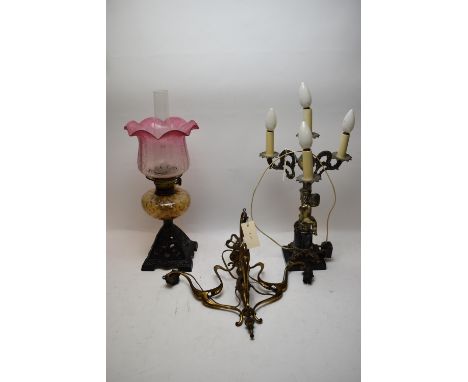 A late Victorian Duplex oil lamp; an Arts &amp; Crafts three-branch chandelier; and a modern putto style table lamp on black 