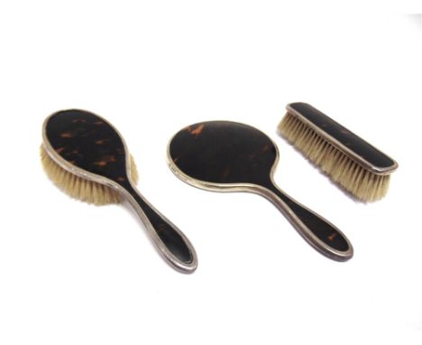 A THREE PIECE SILVER AND TORTOISESHELL DRESSING TABLE SET  comprising a hand mirror and two brushes.