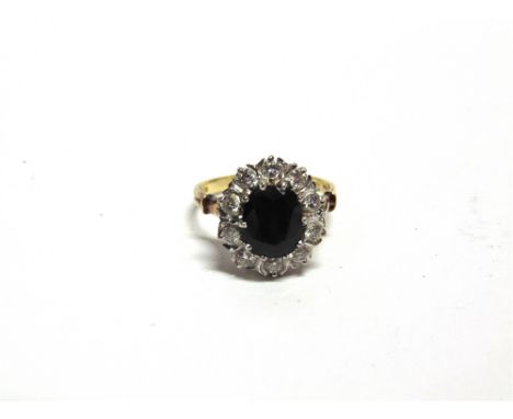 A 18 CARAT GOLD SAPPHIRE AND DIAMOND CLUSTER RING 1976, the oval cut sapphire measuring approximately 8.9mm by 7mm by 4.8mm, 