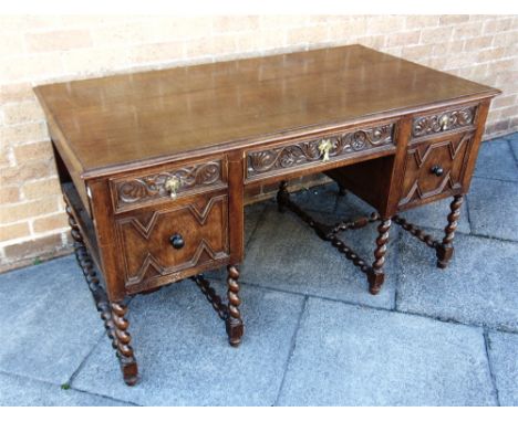 AN EDWARDIAN OAK DESK  with frieze drawer flanked by faux drawers and doors, drawer and open shelf to each end, on barley twi