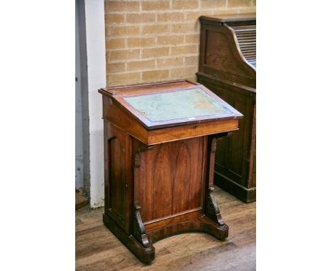 A 19TH CENTURY ROSEWOOD DAVENPORT, the leather inset writing flap above foliate carved corbels, panelled side door enclosing 