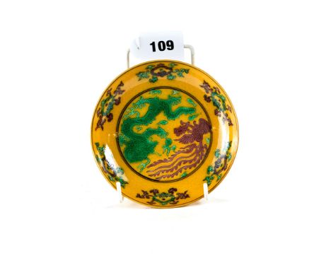 A CHINESE YELLOW GROUND PORCELAIN SAUCER DISH decorated in green/manganese with a five claw dragon and phoenix, bears Qianlon