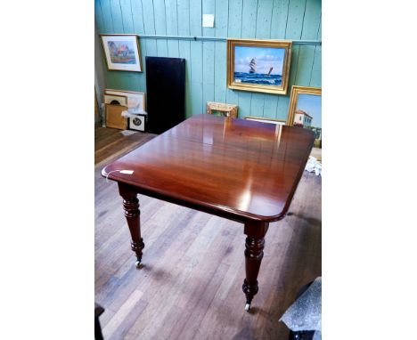 A VICTORIAN STYLE MAHOGANY EXTENDING DINING TABLE, one extra leaf raised on round turned legs with brass and ceramic castors,