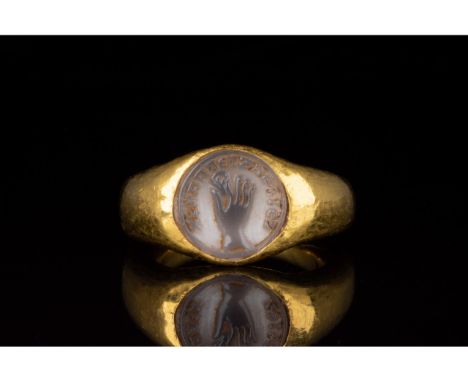 100-300 AD. Roman. Gold ring with circular hoop and rounded bezel containing a grey gemstone intaglio setting. The intaglio f