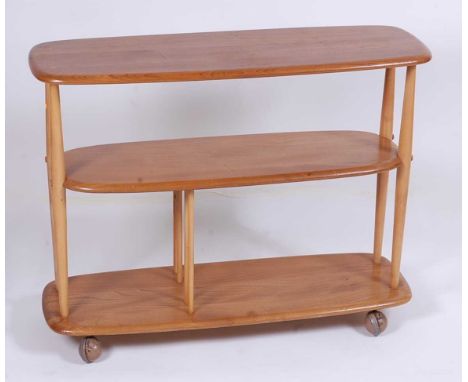 A 1960s Ercol light elm three-tier bookshelf trolley, the tiered surfaces of rounded form, raised on turned supports to rolle