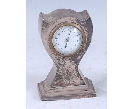 An Art Nouveau silver clad bedside clock, of shaped and pinched form to stepped base, having 2" white enamel dial, winding mo