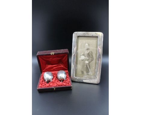 A pair of French silver egg cups, monogrammed in fitted case, 90g, together with a white metal mounted easel photograph frame