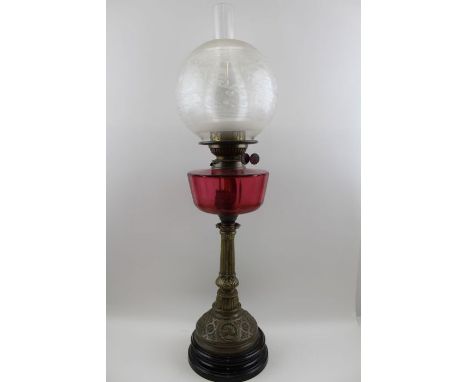 A late Victorian oil lamp with cranberry reservoir, raised upon a decorative brass stem, complete with etched globe shade, an