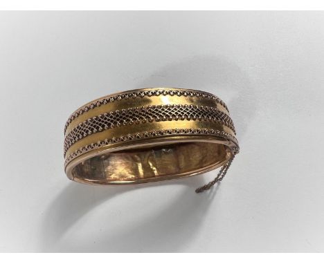 A yellow metal bangle with fancy embossed central border and rims to one side, the other side plain (back dented and repaired