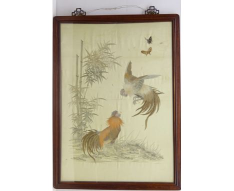 Chinese framed silk embroidered panel depicting two fighting cockerels beside bamboo and butterflies, on ivory ground, in har