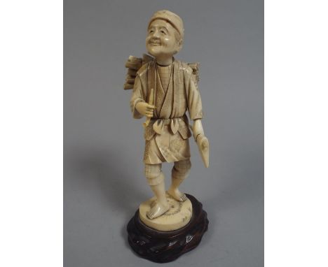 An Early 20th Century Ivory Okimono Figure of an Elderly Wood Cutter Holding an Axe and Pipe. Mounted on a Wooden Plinth. 