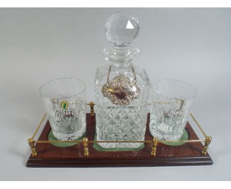 A Whiskey Decanter, Plated Label and Pair of Waterford Crystal Glasses on Brass Galleried Mahogany Plinth. 