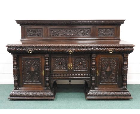 A large Victorian profusely carved oak sideboard, the low carved back over three gadroon moulded frieze drawers fitted with b