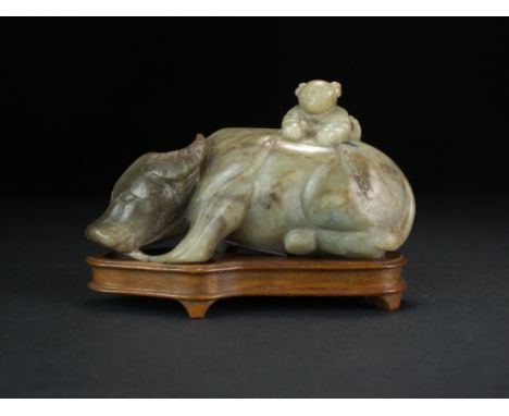 A Chinese grey-green jade carving of a water buffalo, Qing Dynasty, the beast modelled recumbent with a confucian boy sitting