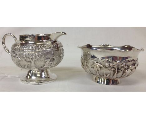 WHITE METAL SUGAR BASIN AND CREAM JUG DECORATED WITH PALM TREES AND FIGURES 
