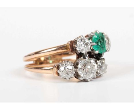 A gold, diamond and emerald ring in a twin shank design, claw set with five old cut diamonds and an emerald, unmarked, weight