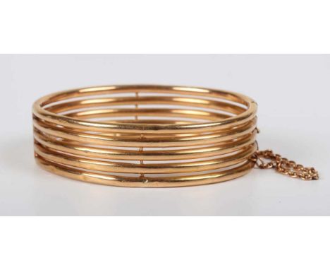 A gold oval hinged bangle in a five row tubular design, on a snap clasp, fitted with a safety chain, unmarked, weight 22.3g, 