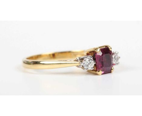 An 18ct gold, ruby and diamond ring, claw set with a cut cornered rectangular step cut ruby between two circular cut diamonds