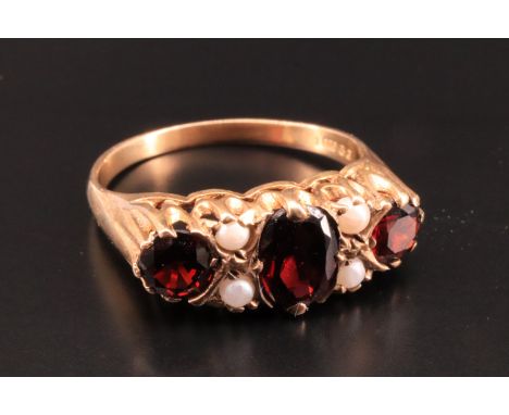 A vintage garnet and pearl ring, comprising a central oval garnet of approximately 7 mm x 5 mm, set between a pair of circula